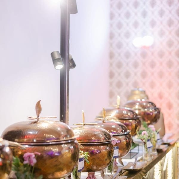 A buffet line with several ornate copper chafing dishes and serving utensils on a decorated table.