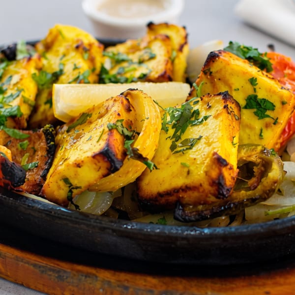 Sizzling paneer tikka with bell peppers, onions, and cilantro, served on a cast iron platter.