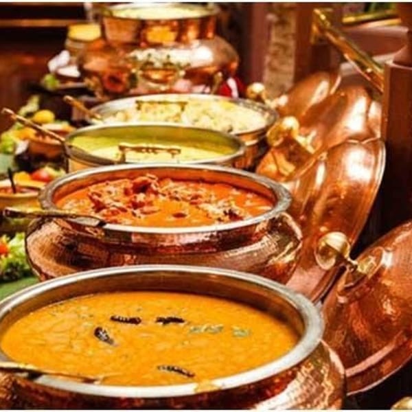 A buffet line of Indian curries and dishes in ornate copper serving pots.