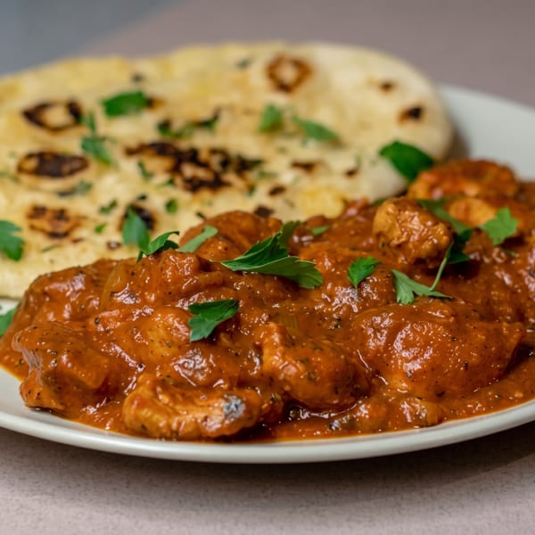 Chicken tikka masala with naan bread, garnished with fresh parsley on a white plate.